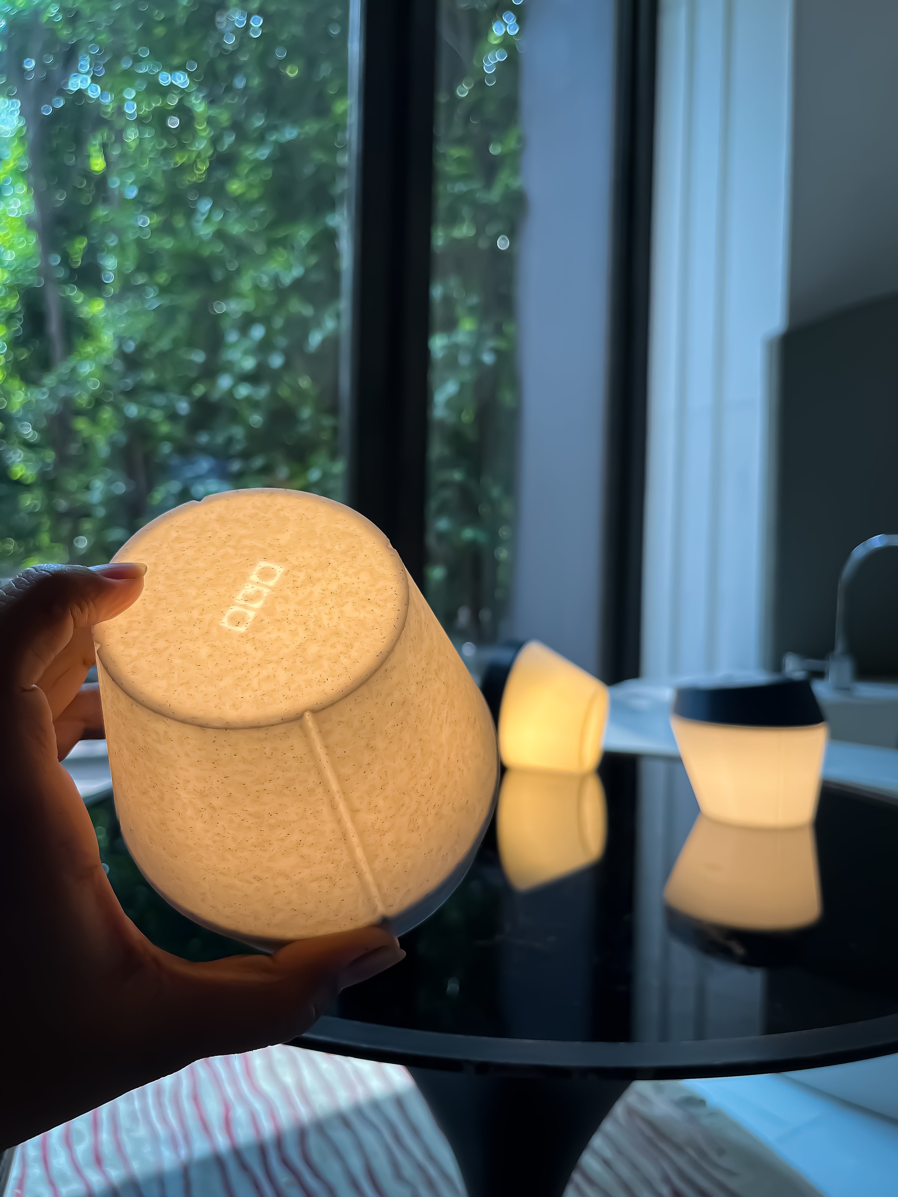 A customizable portable lamp featuring the 'One Good Object' logo, set against the blurred backdrop of a personal bathroom space with a bathtub, evoking a sense of sophistication.