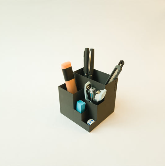 Grey cube pen holder with office supplies on a white background