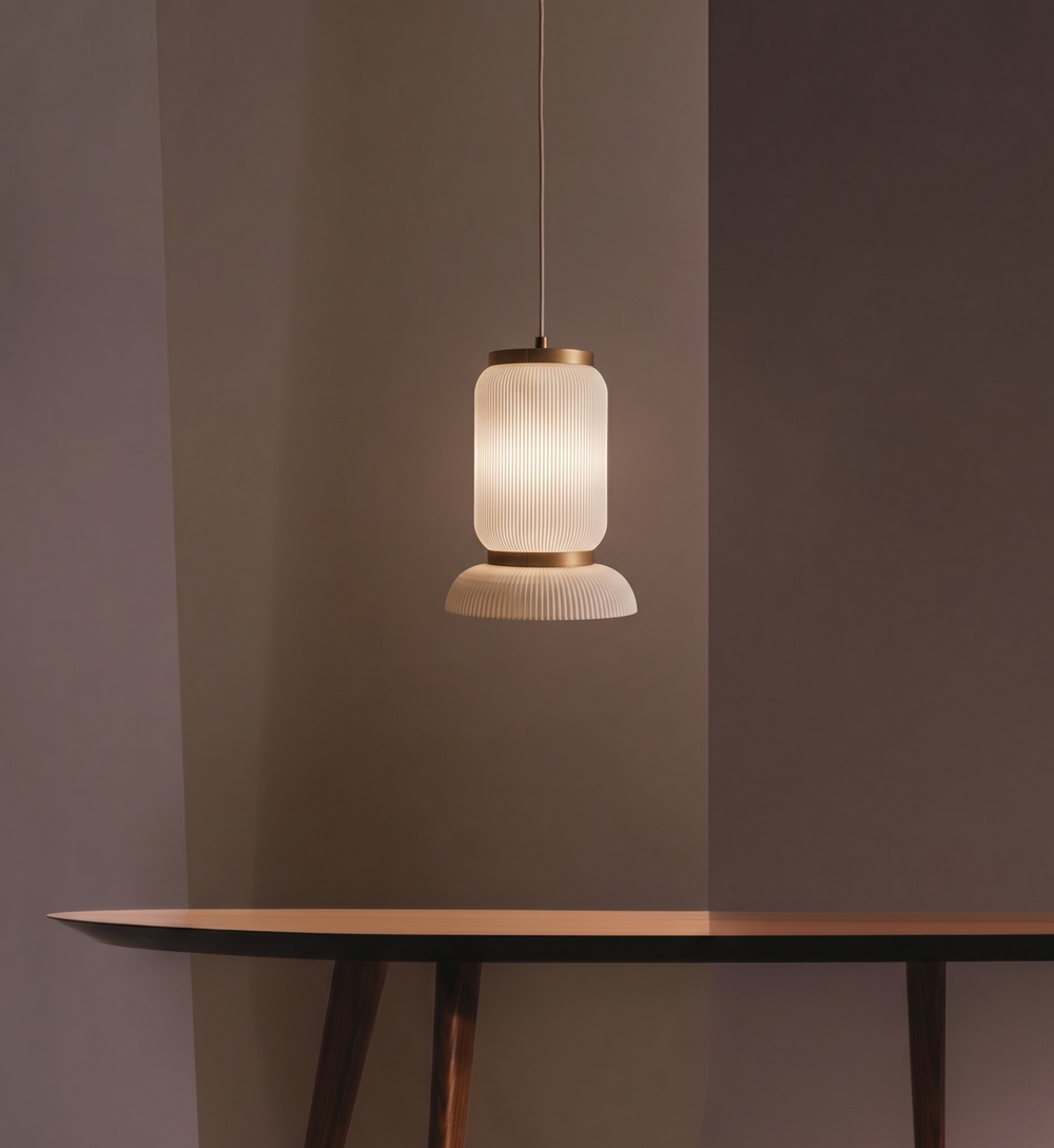 The Bello S pendant lamp emitting a warm, diffused glow, featuring a vertically ribbed cylindrical body, elegant brass accents, and a flared ribbed bottom shade.