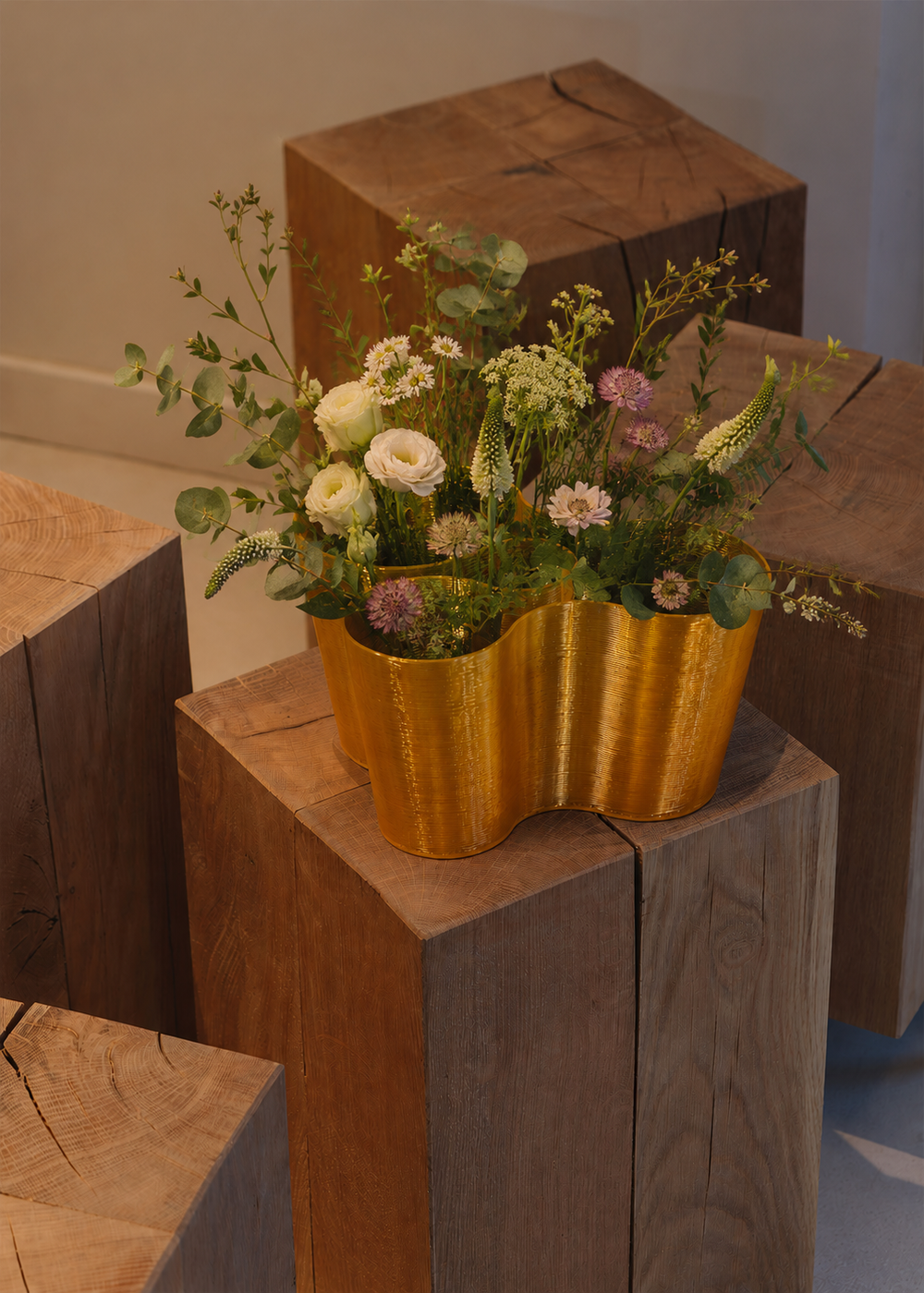 The Coral Crest Stand acting as a modern vase, showcasing a continuous,organic curved silhouette with a textured gold finish, filled with lush greenery and delicate blooms.