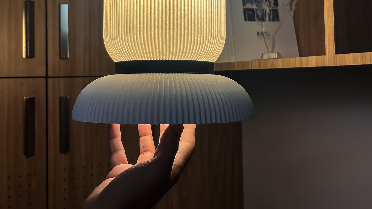 Hand holding Ganta a textured pendant lampshade against a wooden cabinet background