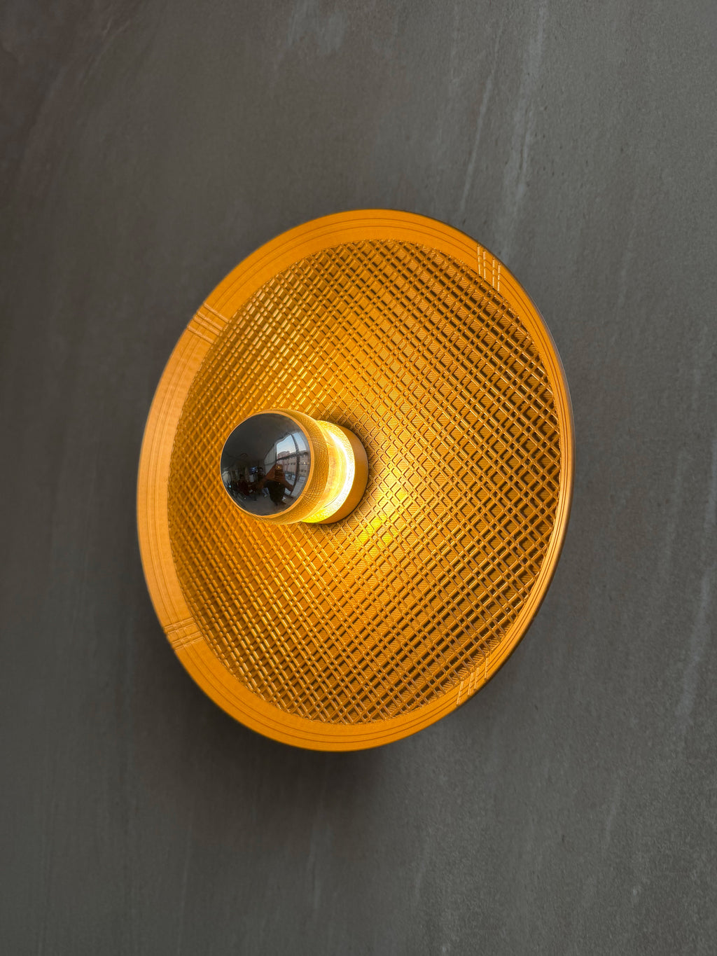 Side angled on shot of Ora wall light with textured surface and a reflector bulb on a gray background