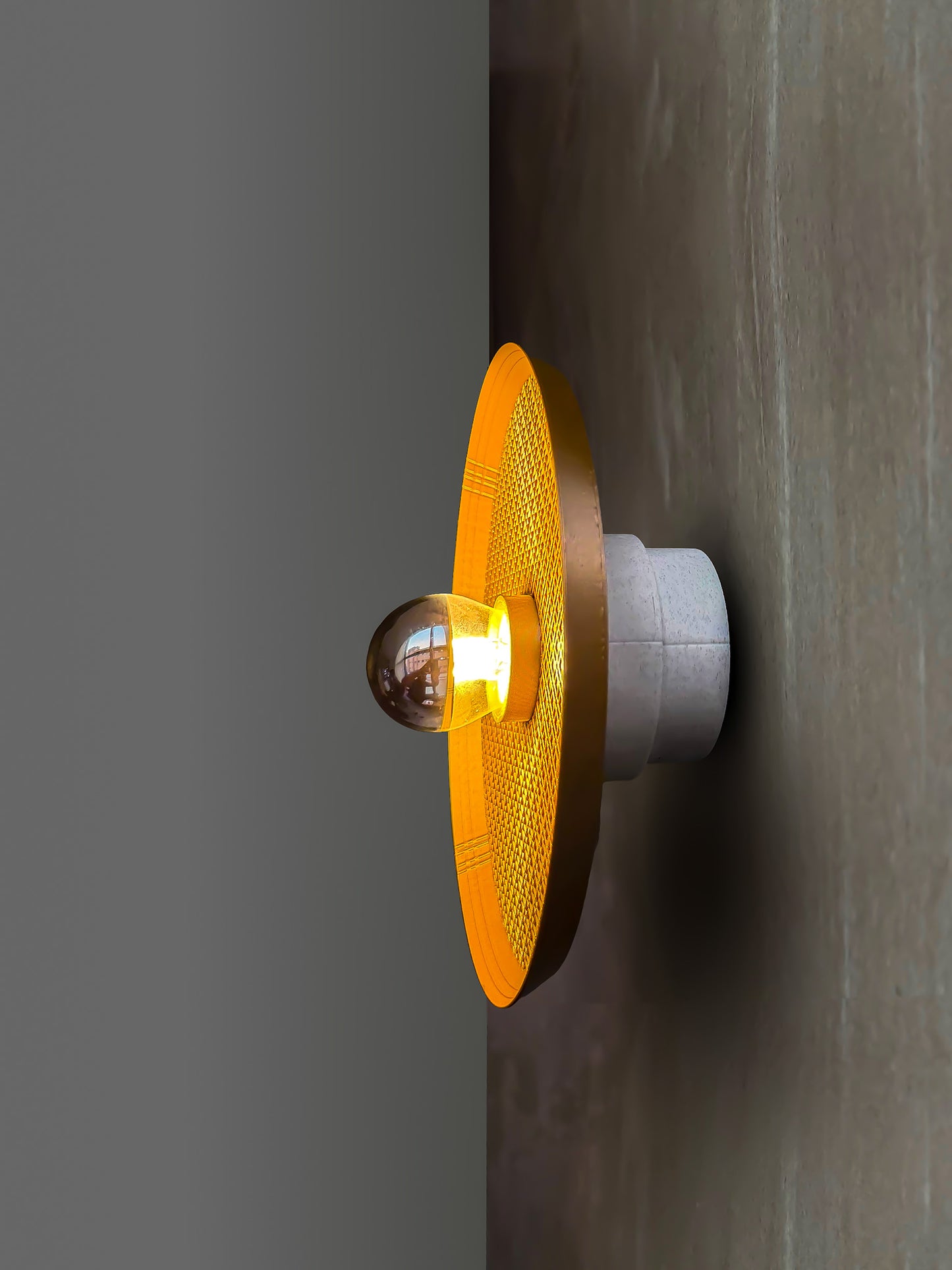 side angle of Ora wall light with textured surface and a reflector bulb on a gray background
